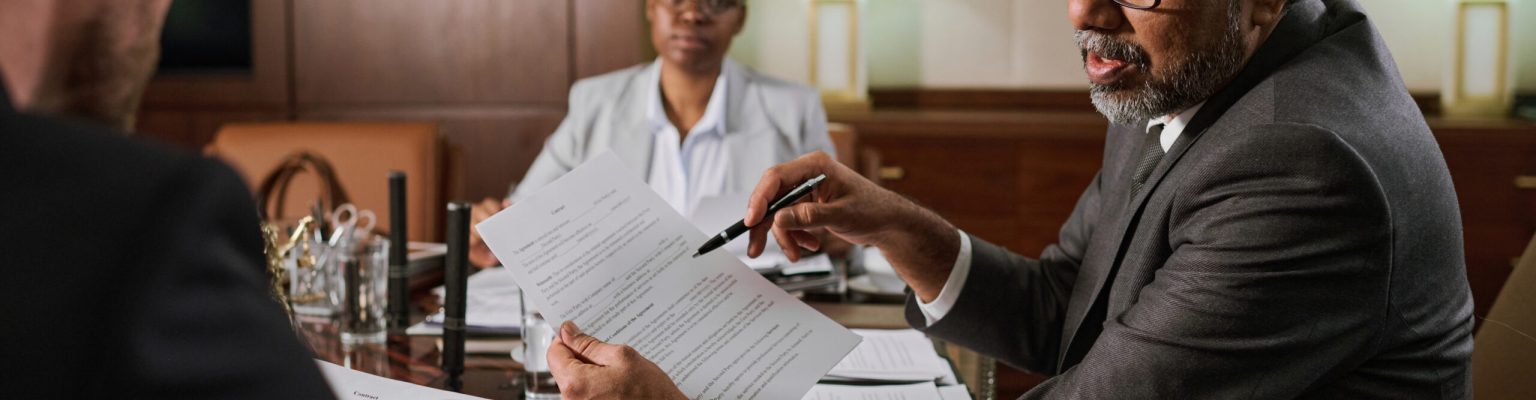 Mature male boss or chief executive officer with paper document in hands looking at younger colleague during explanation of contract points